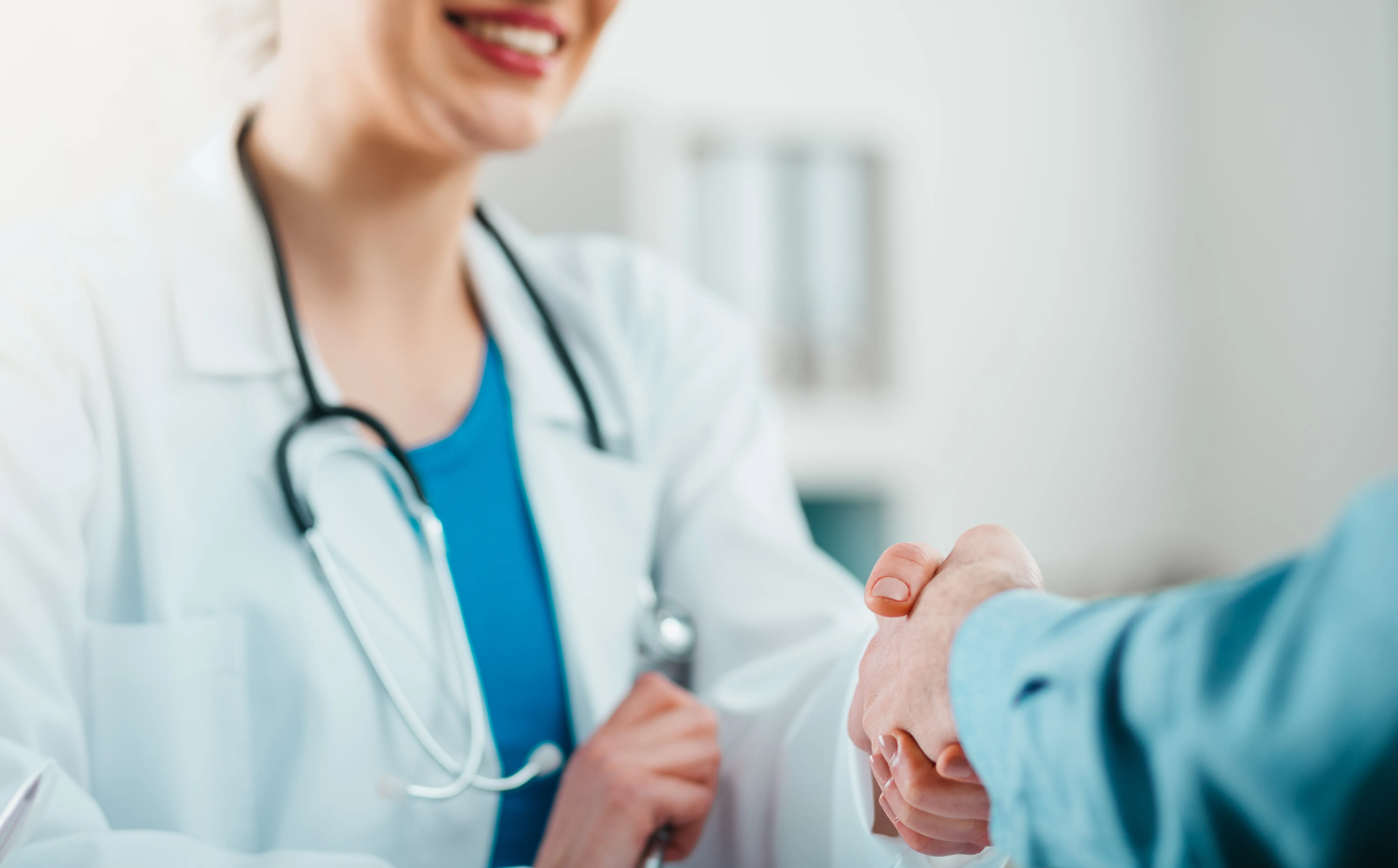 A clinician in a white coat and stethoscope examining a patient’s forearm