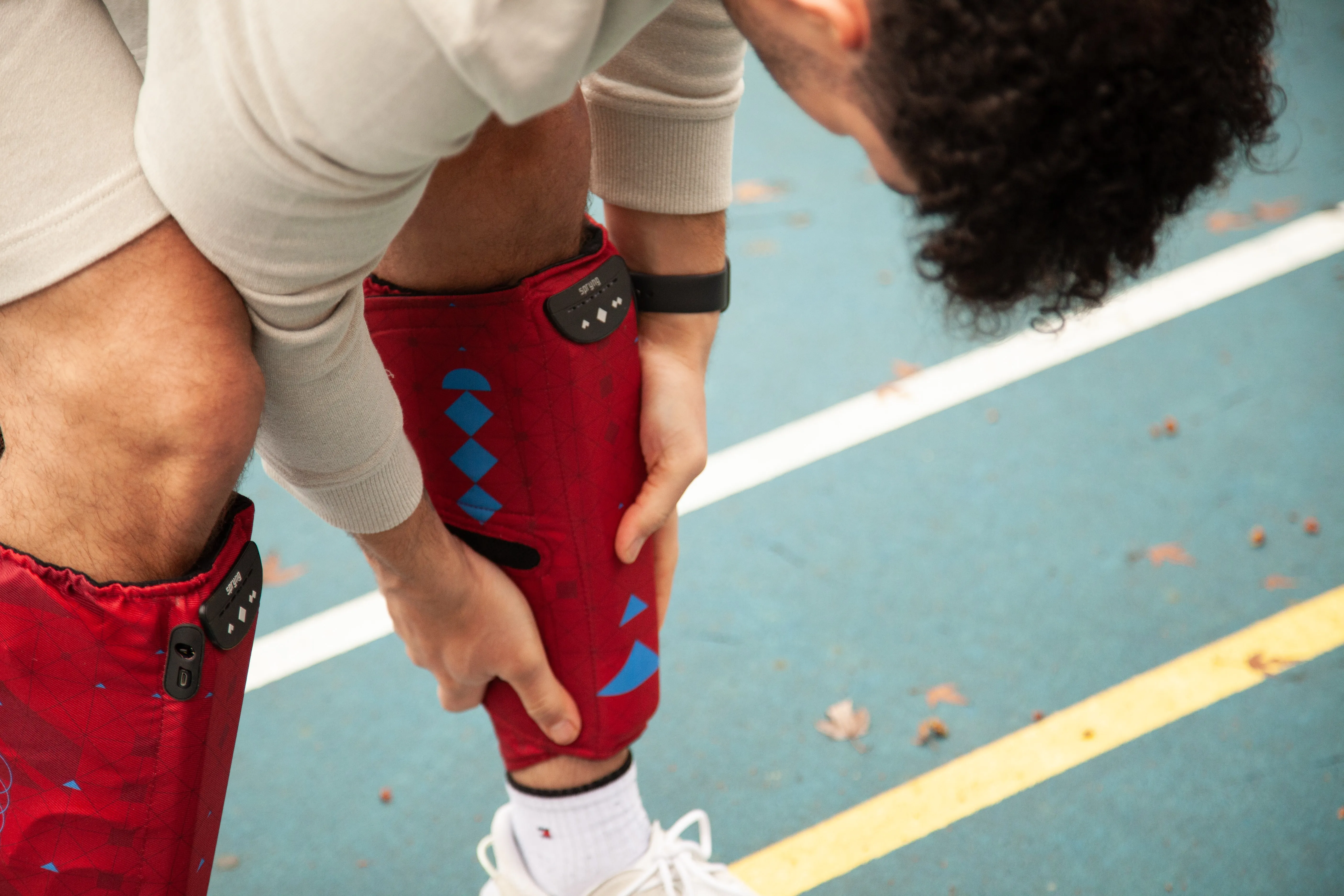 An athlete bending to adjust a compression sleeve on their calf on a track