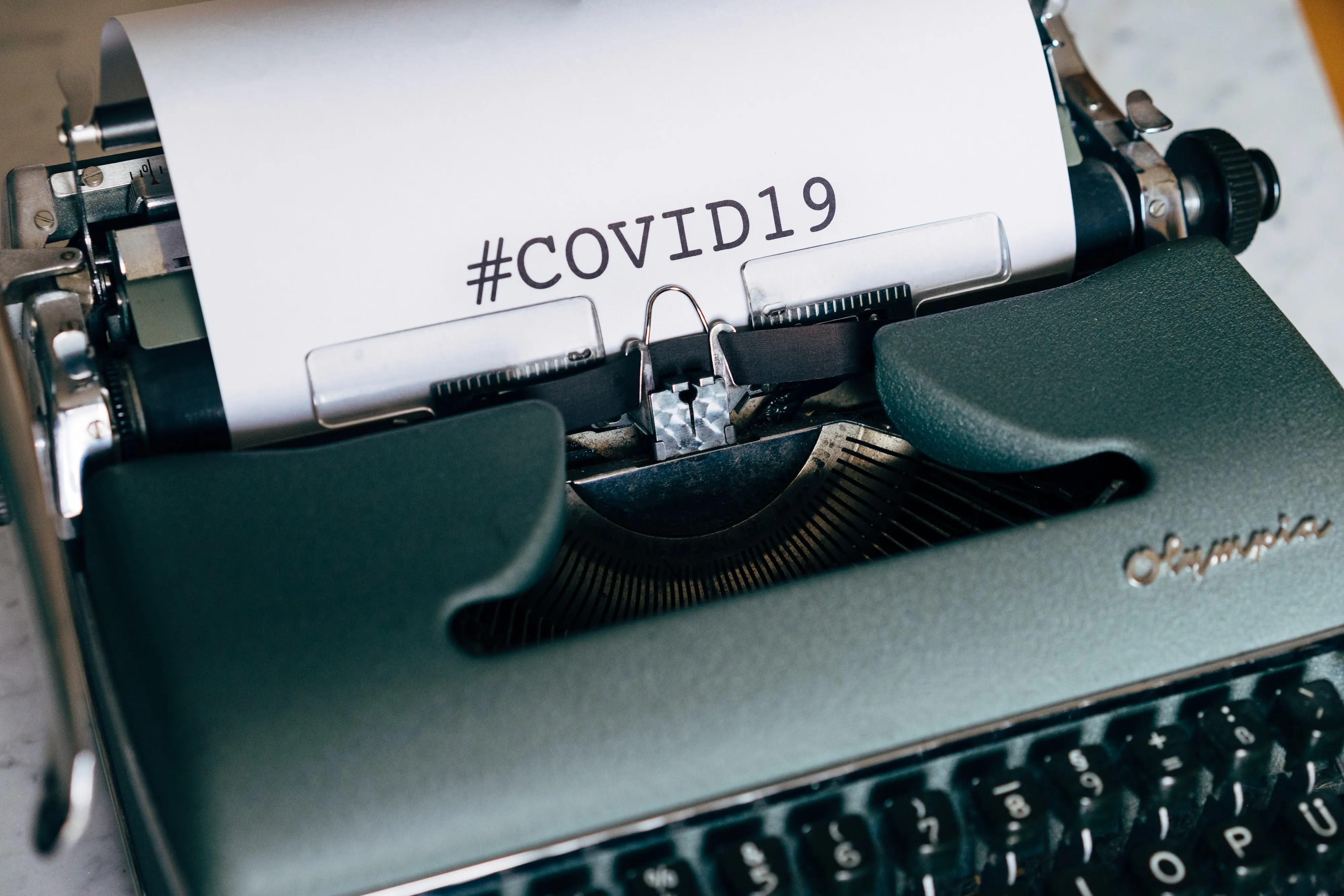 A sheet of paper in a typewriter carriage printed with the hashtag #COVID19