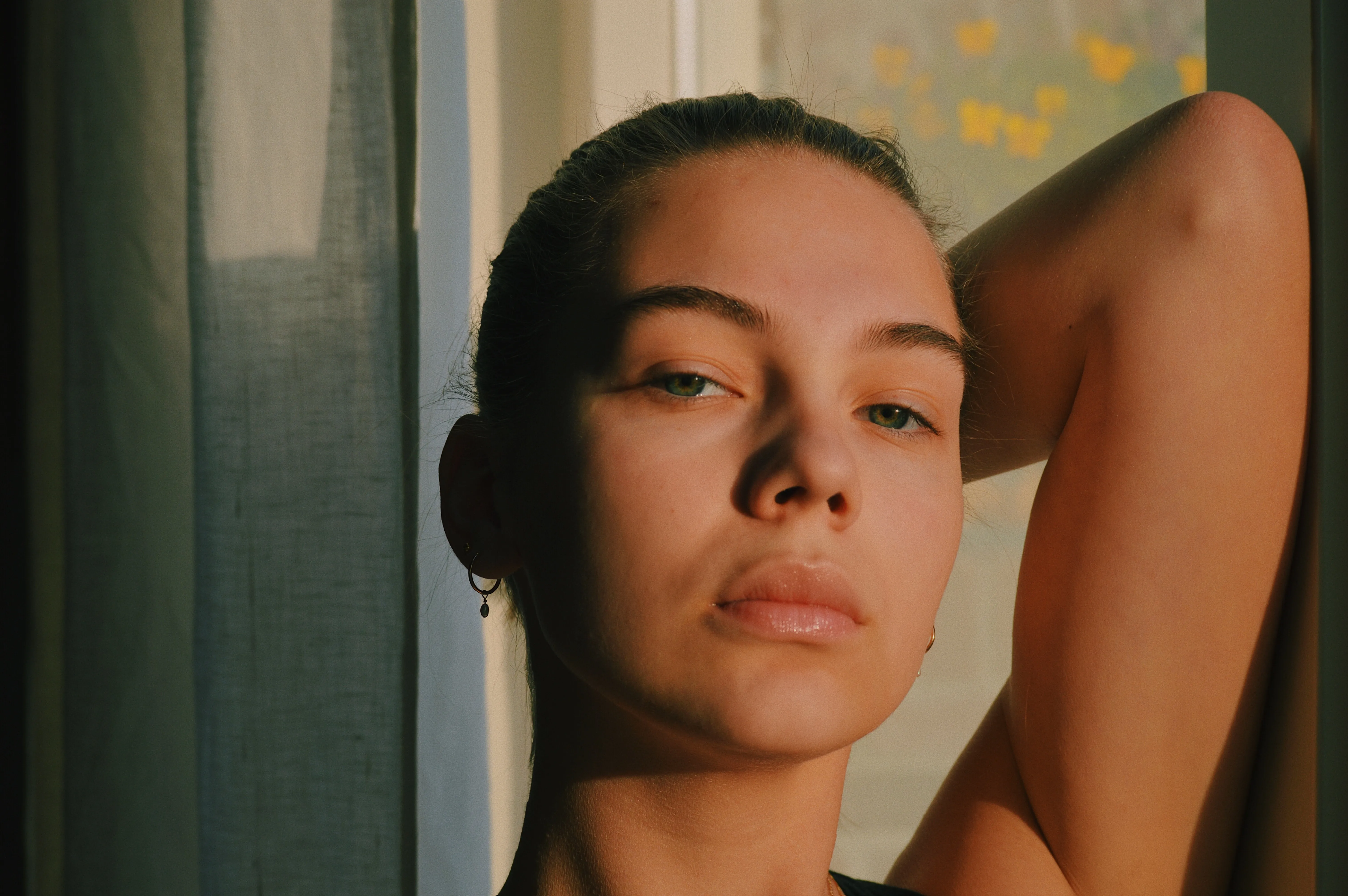A woman with bare, clear skin resting beside a sunlit window