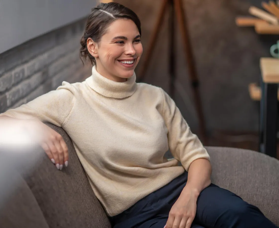 A woman sitting comfortably on a sofa at home, smiling
