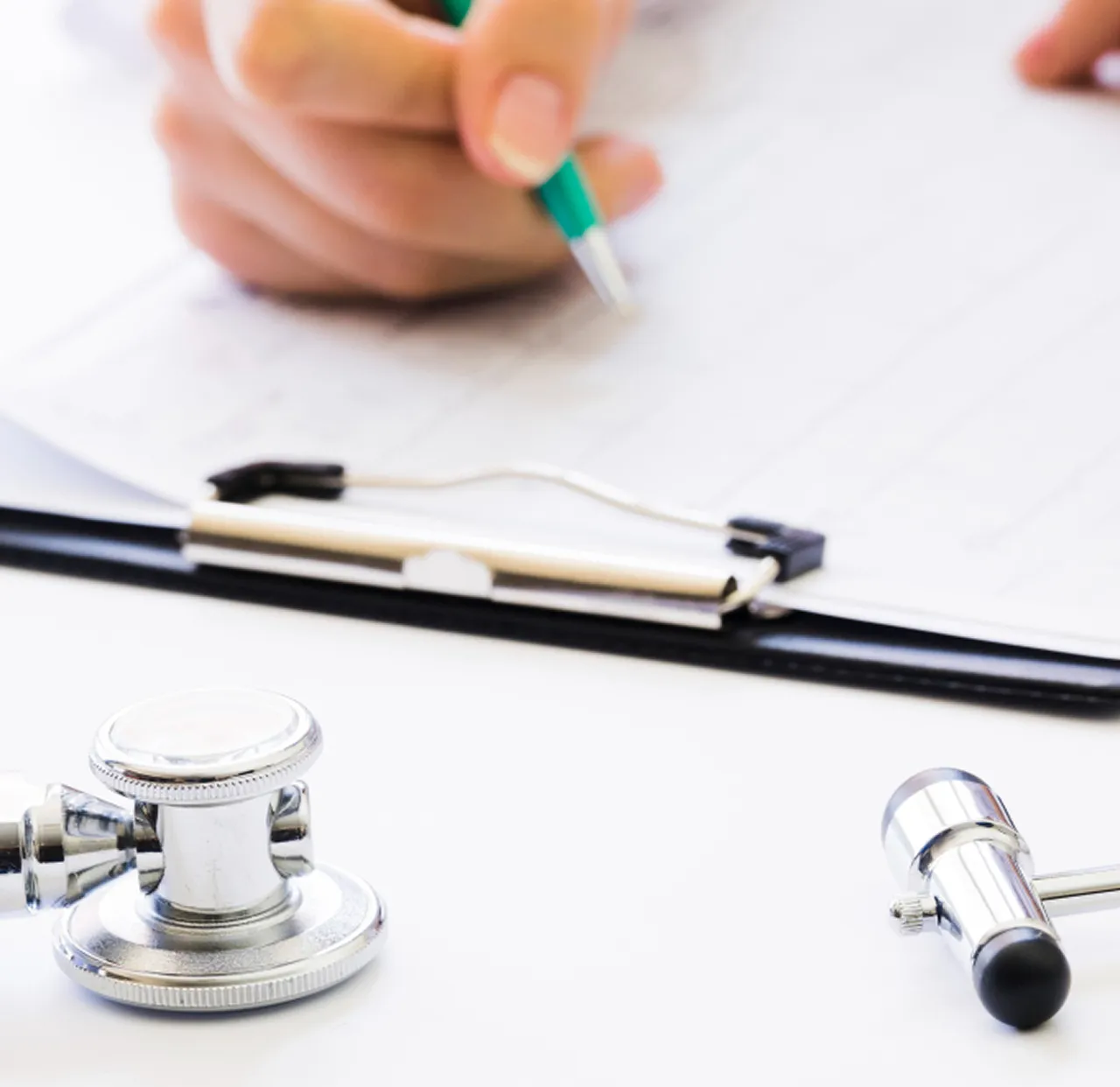 A clinician writing up results beside a stethoscope and blood pressure cuff