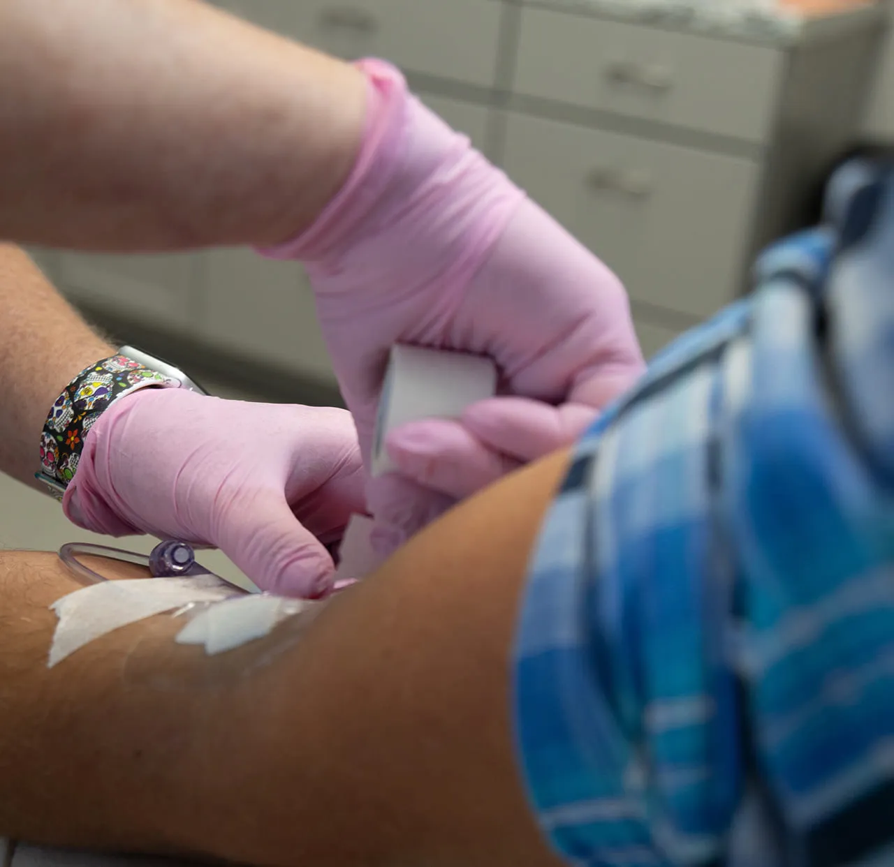 Gloved hands securing an IV line to a patient’s arm