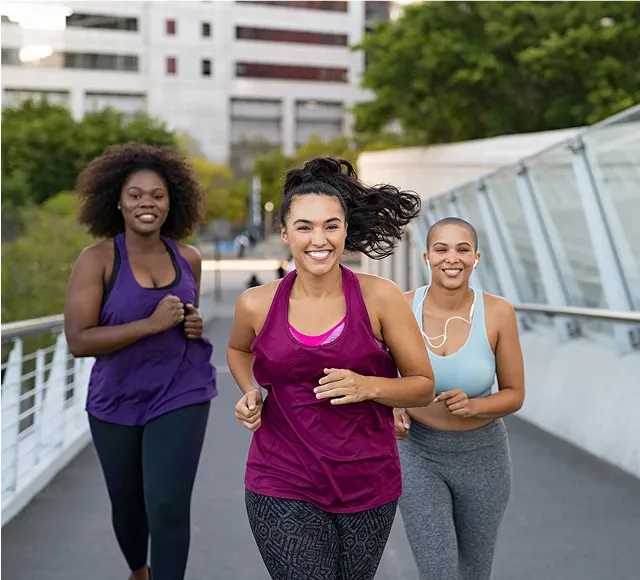 Three women running together across a city bridge