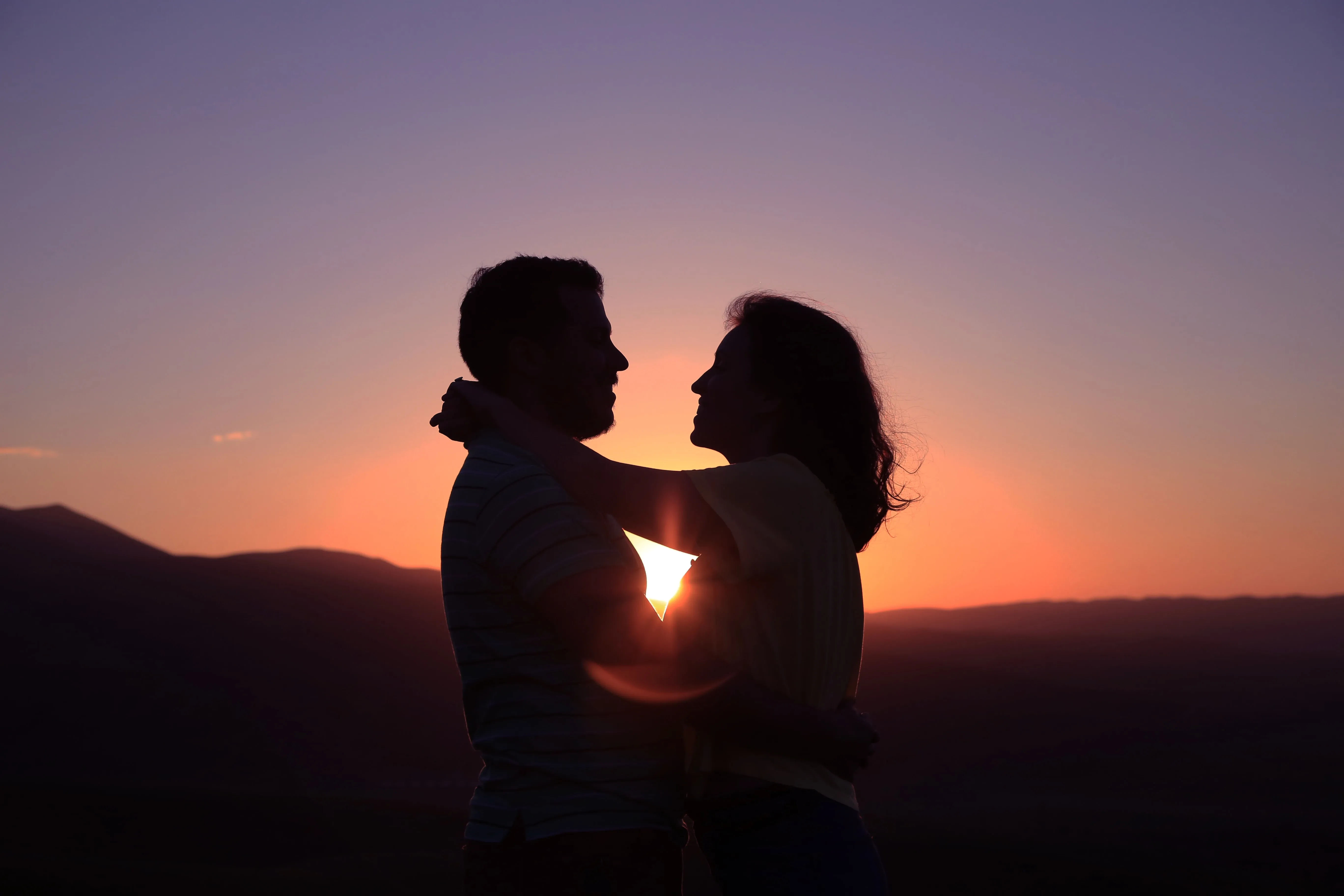 A couple standing face to face in silhouette against a sunset