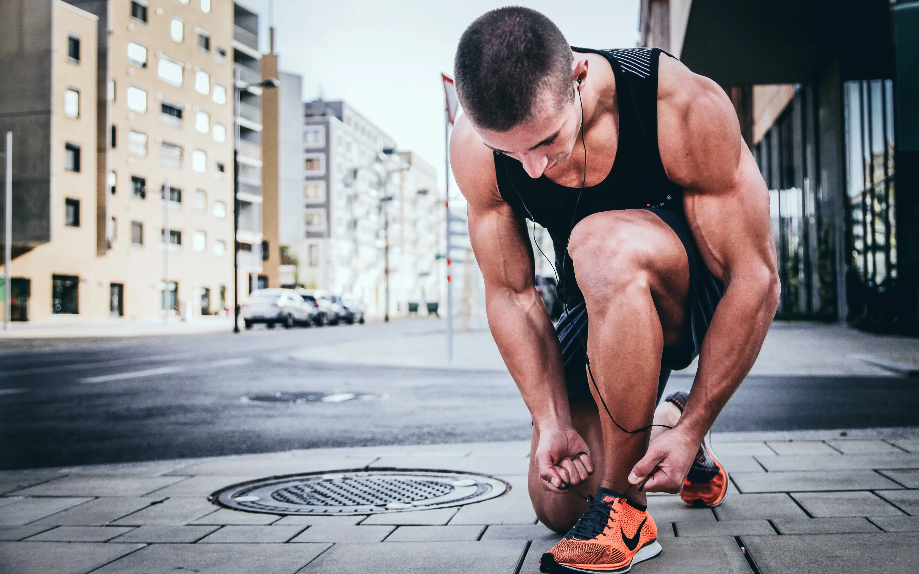 A man in running kit crouching to tie his shoe on a city street