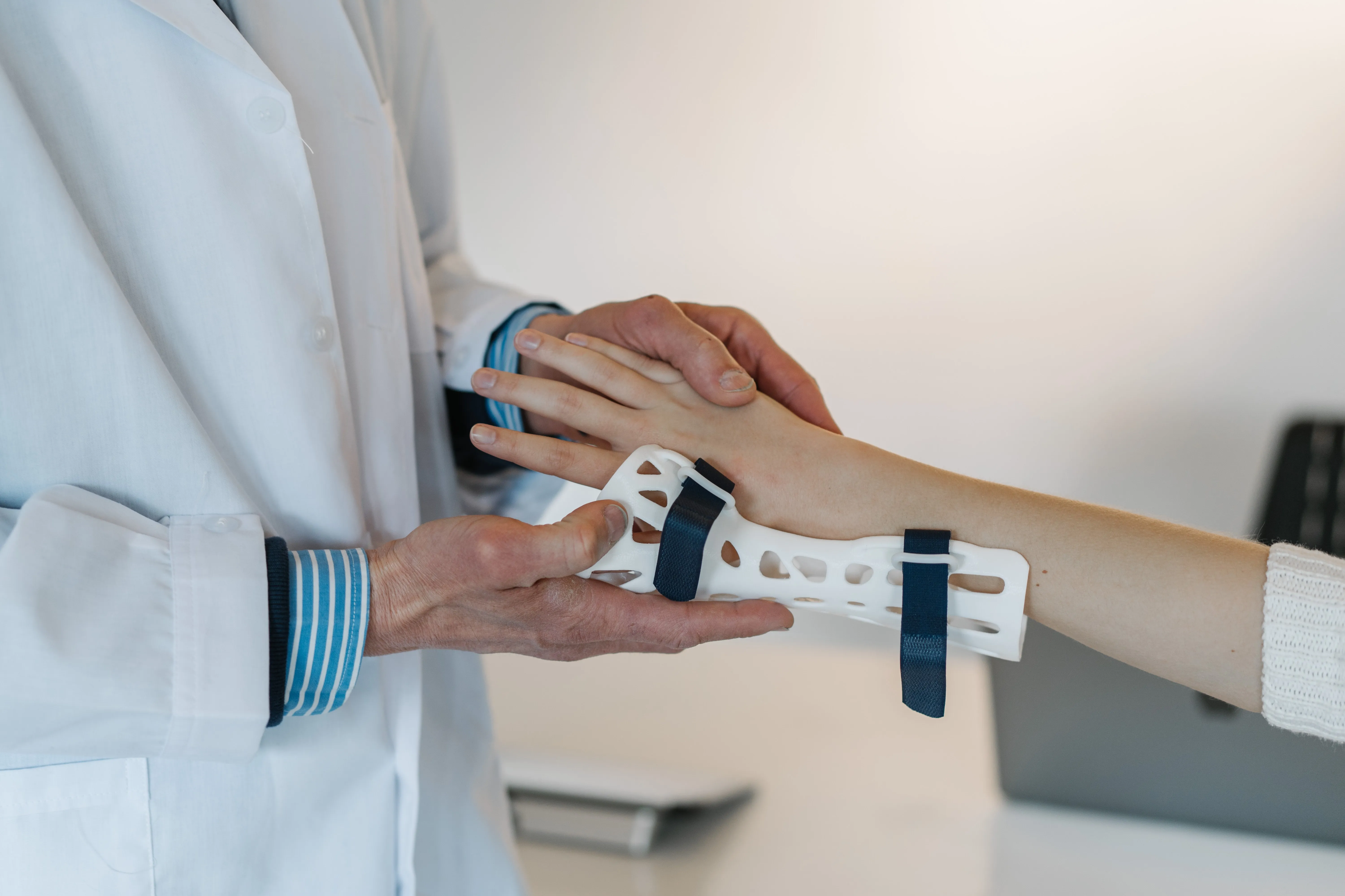 A clinician in a white coat fitting a wrist splint to a patient’s arm