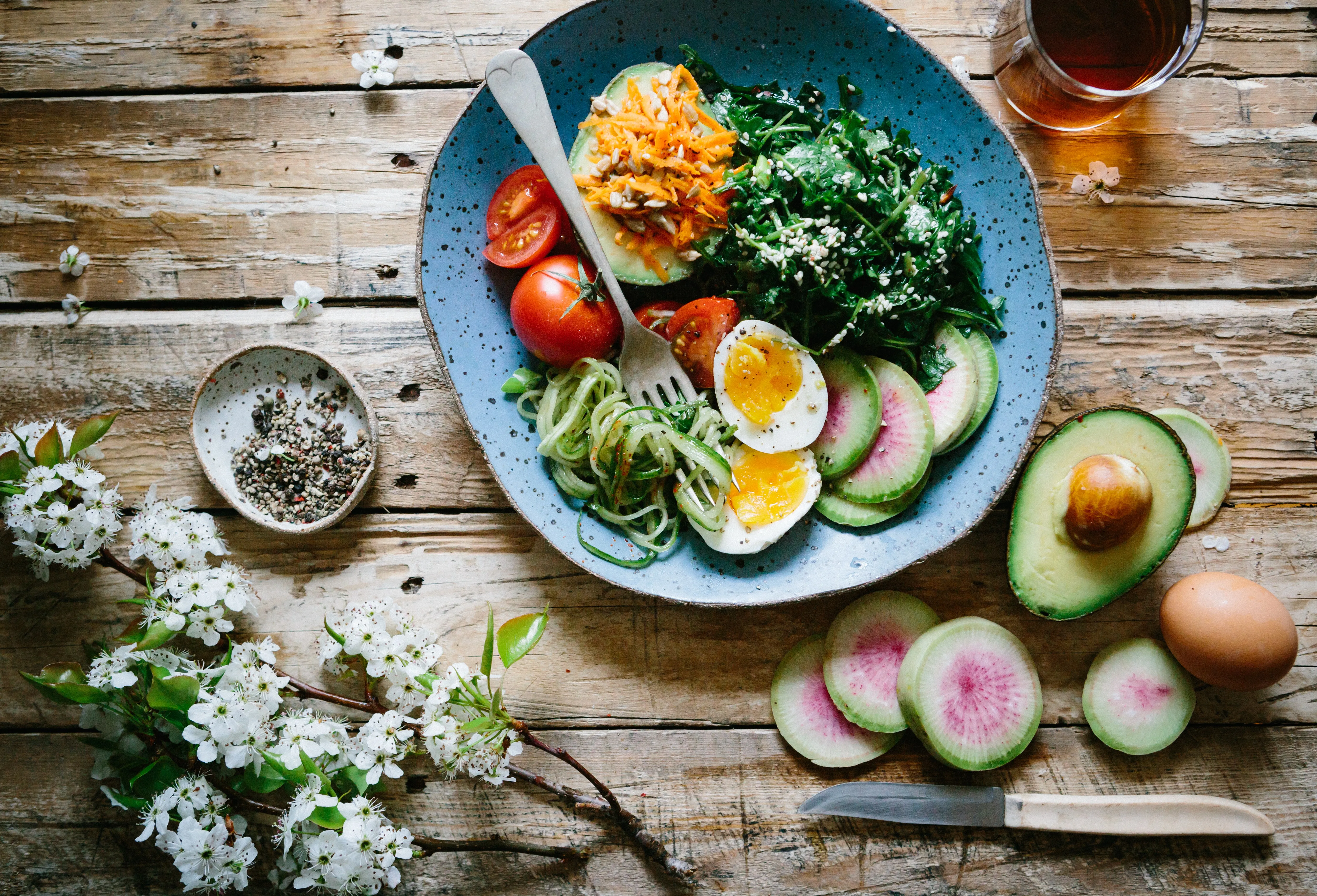 A bowl of salad with egg, avocado and tomato beside sliced radish on a wooden table