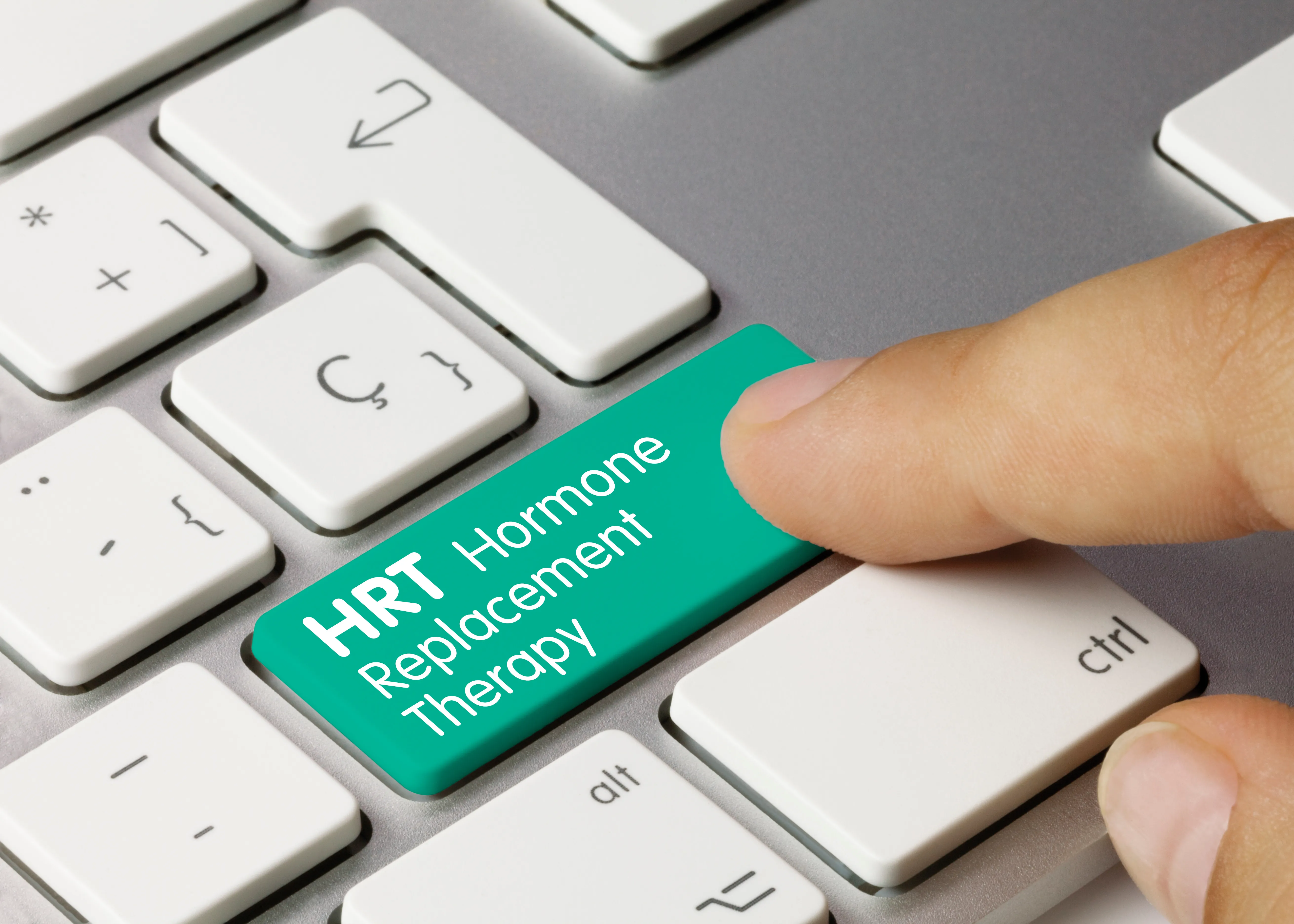 A finger pressing a green keyboard key labelled HRT, Hormone Replacement Therapy